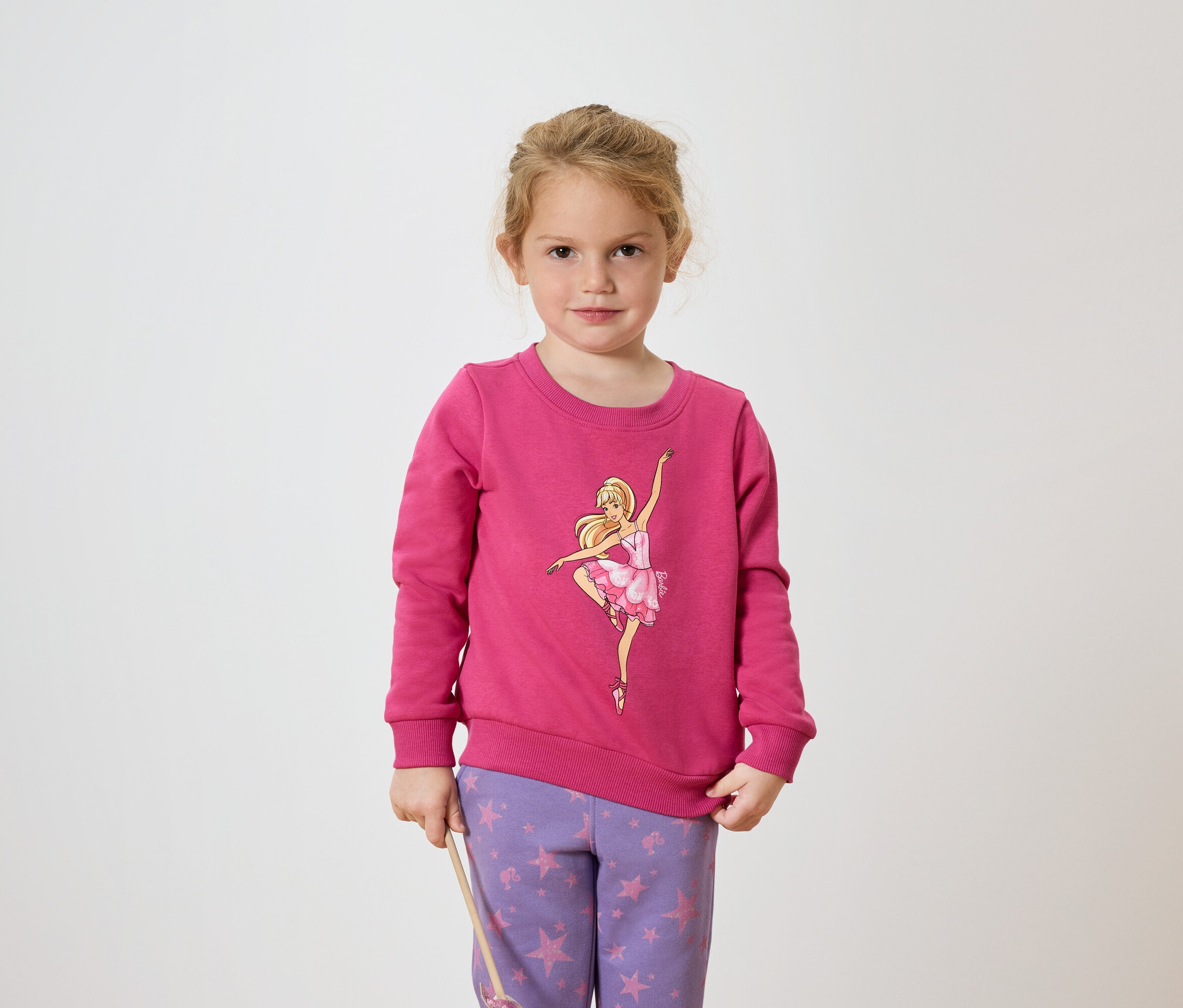 Fillette portant un pull rose avec une ballerine et un pantalon violet à motifs d'étoiles.
