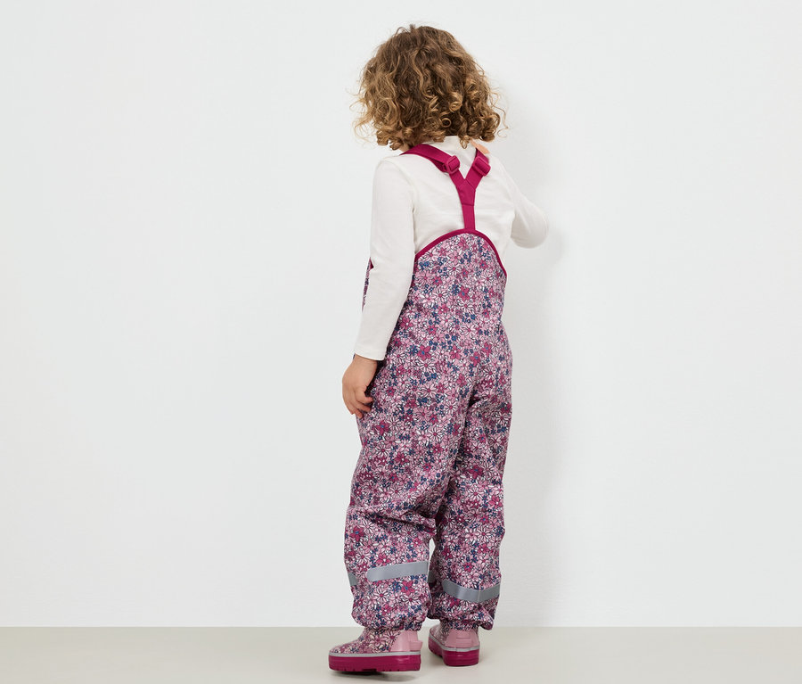 Une fillette portant une salopette fleurie et des bottes roses, dos à la caméra.