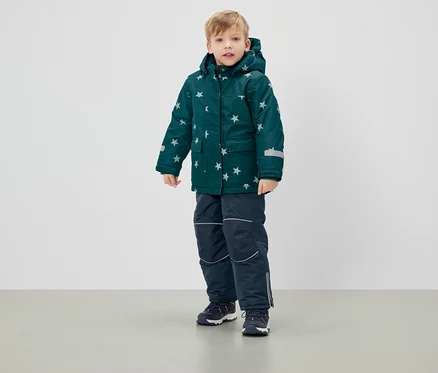 Garçon debout portant une veste d'hiver verte à étoiles et un pantalon bleu marine.