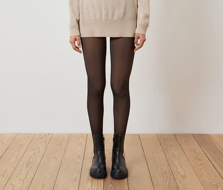 Jambes d'une femme portant des collants noirs et des bottes noires sur un plancher en bois.