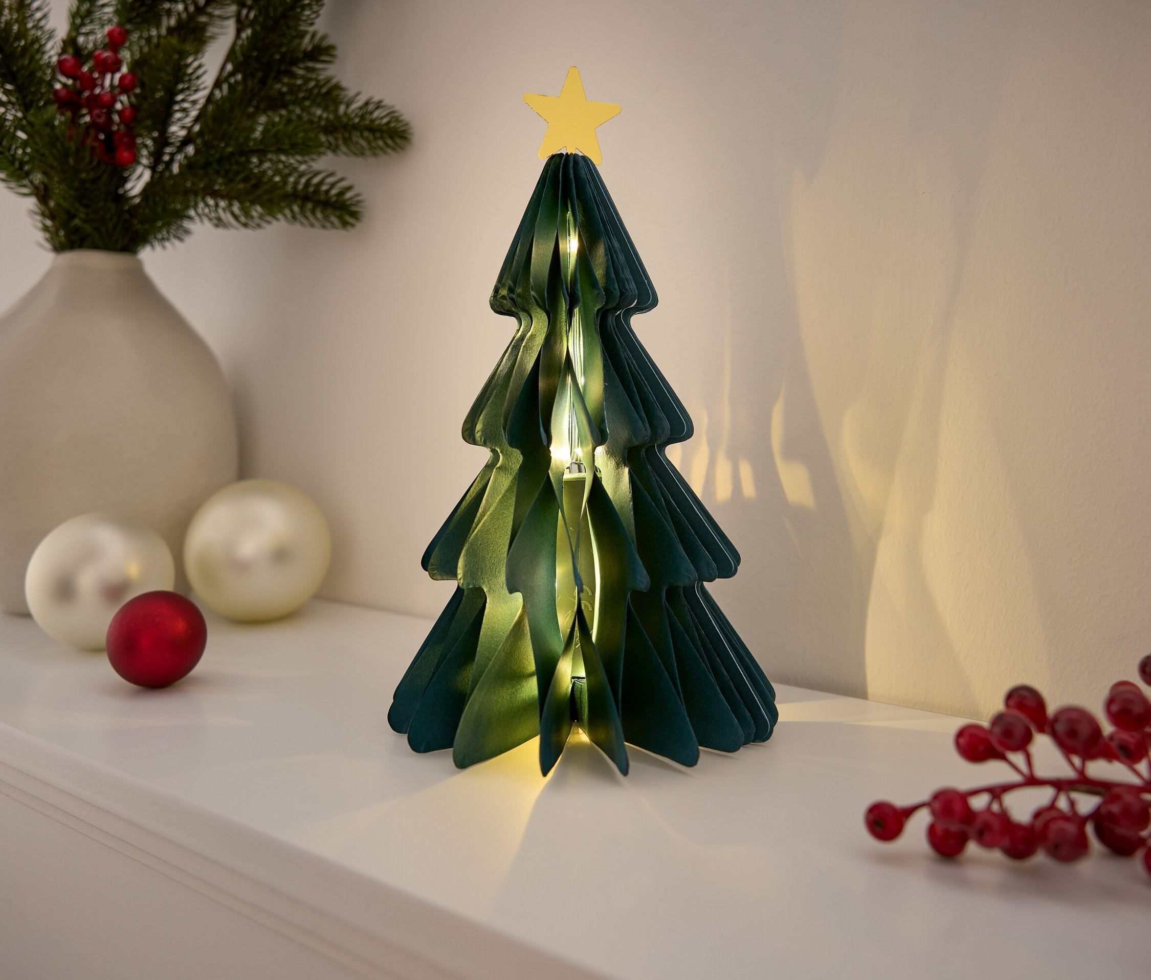 Sapin de Noël décoratif en papier avec étoile sur une étagère blanche.