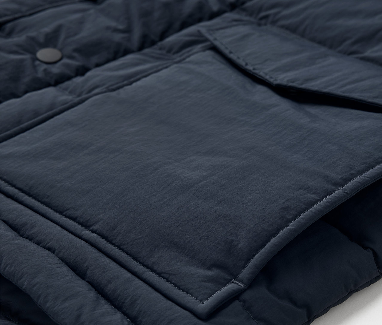Gros plan sur un gilet matelassé bleu marine avec une poche et des boutons.