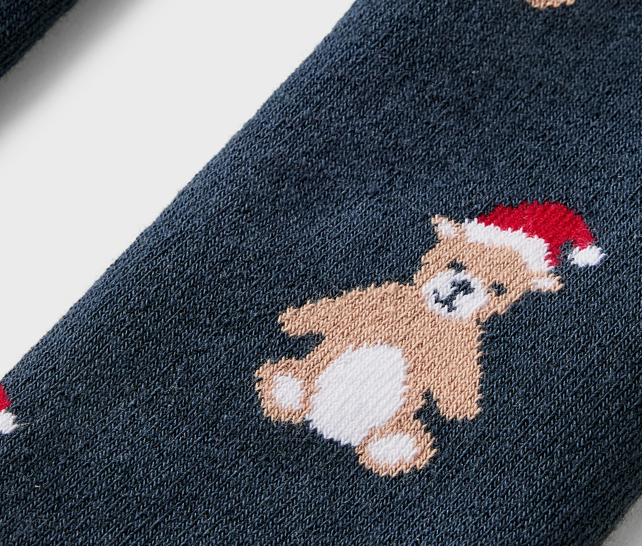 Gros plan d'une chaussette bleue ornée d'oursons coiffés de bonnets de Noël rouges.