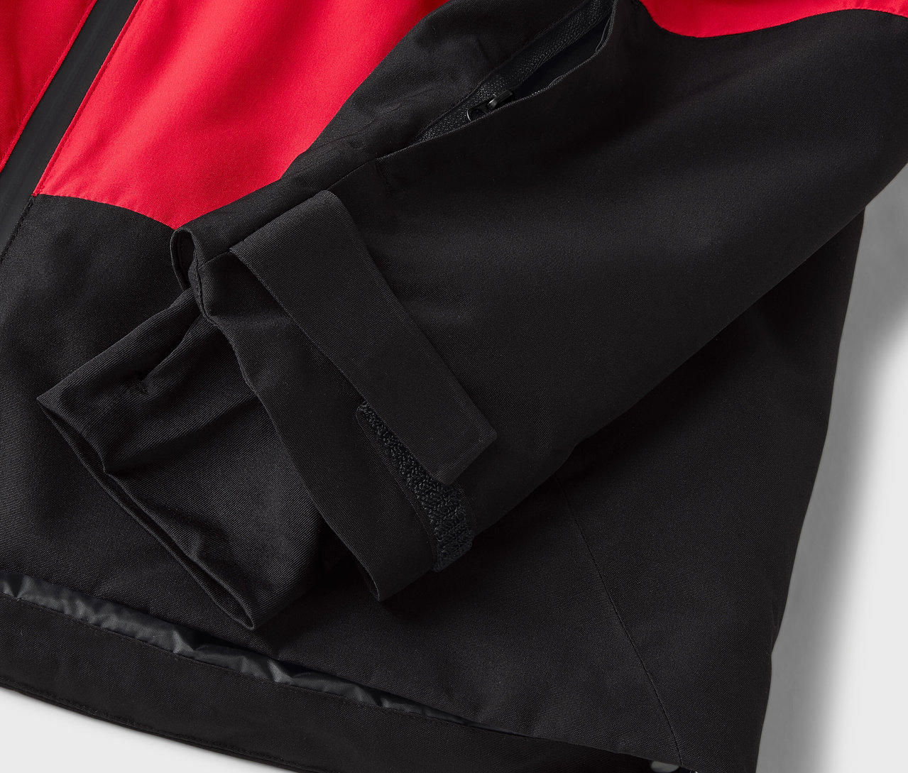 Gros plan sur une manche à velcro d'une veste rouge et noire.