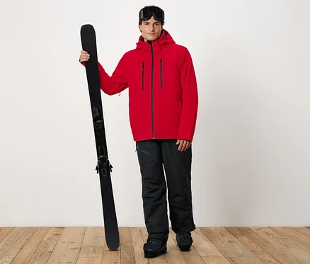 Un homme en veste rouge tenant des skis.