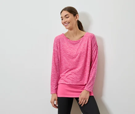 Une femme souriante pose dans un haut rose à manches longues et un legging noir.