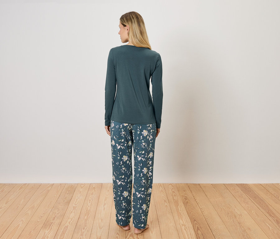Une femme, vue de dos, porte un pyjama vert à manches longues et un pantalon à fleurs.