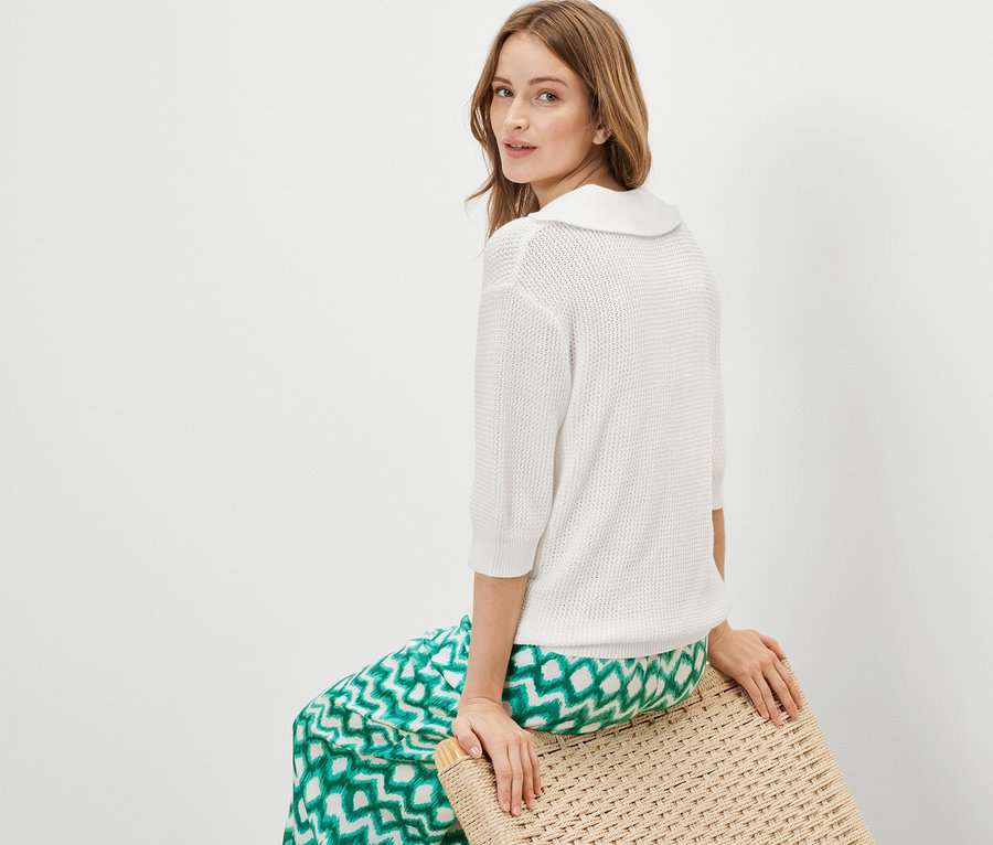 Femme assise sur un tabouret portant un pull d’été en maille blanc.