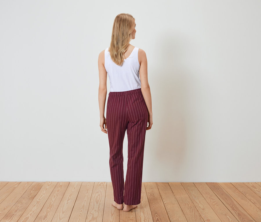 Une femme, vue de dos, porte un débardeur blanc et un pantalon rayé bordeaux.