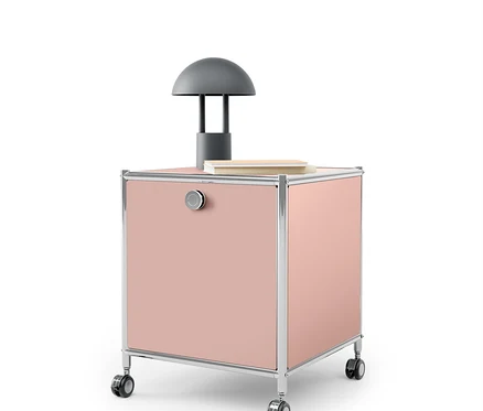 Un caisson rose à roulettes avec un cadre chromé et une lampe grise dessus.
