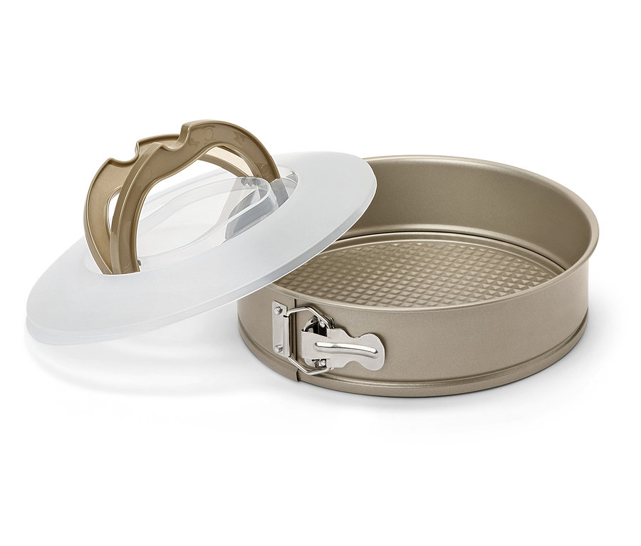 Un moule à manqué doré avec fond amovible et couvercle transparent est posé sur un fond blanc.
