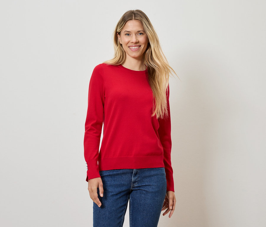 Femme blonde posant en pull rouge et jean bleu.