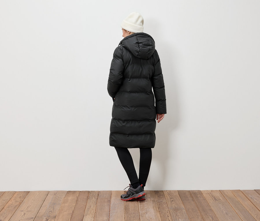 Une femme, vue de dos, porte une doudoune noire, des leggings noirs et un bonnet blanc.