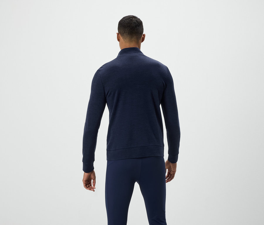 Homme de dos, portant un pull bleu et un pantalon.