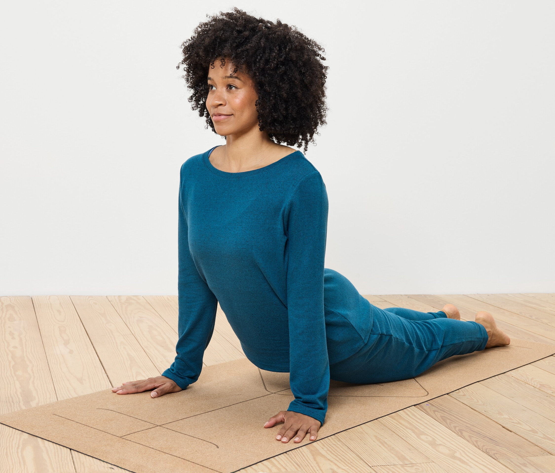 Femme aux cheveux bouclés faisant du yoga dans des vêtements bleus sur un tapis.