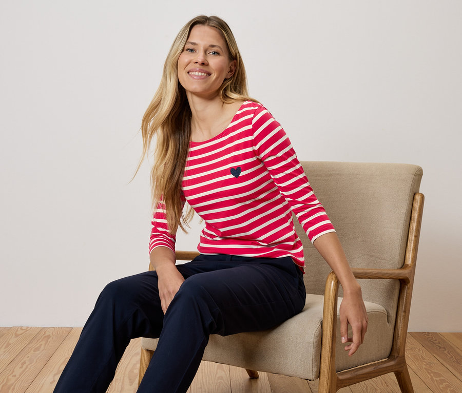 Une femme est assise sur une chaise et porte un t-shirt rayé rouge et blanc et un pantalon bleu marine.
