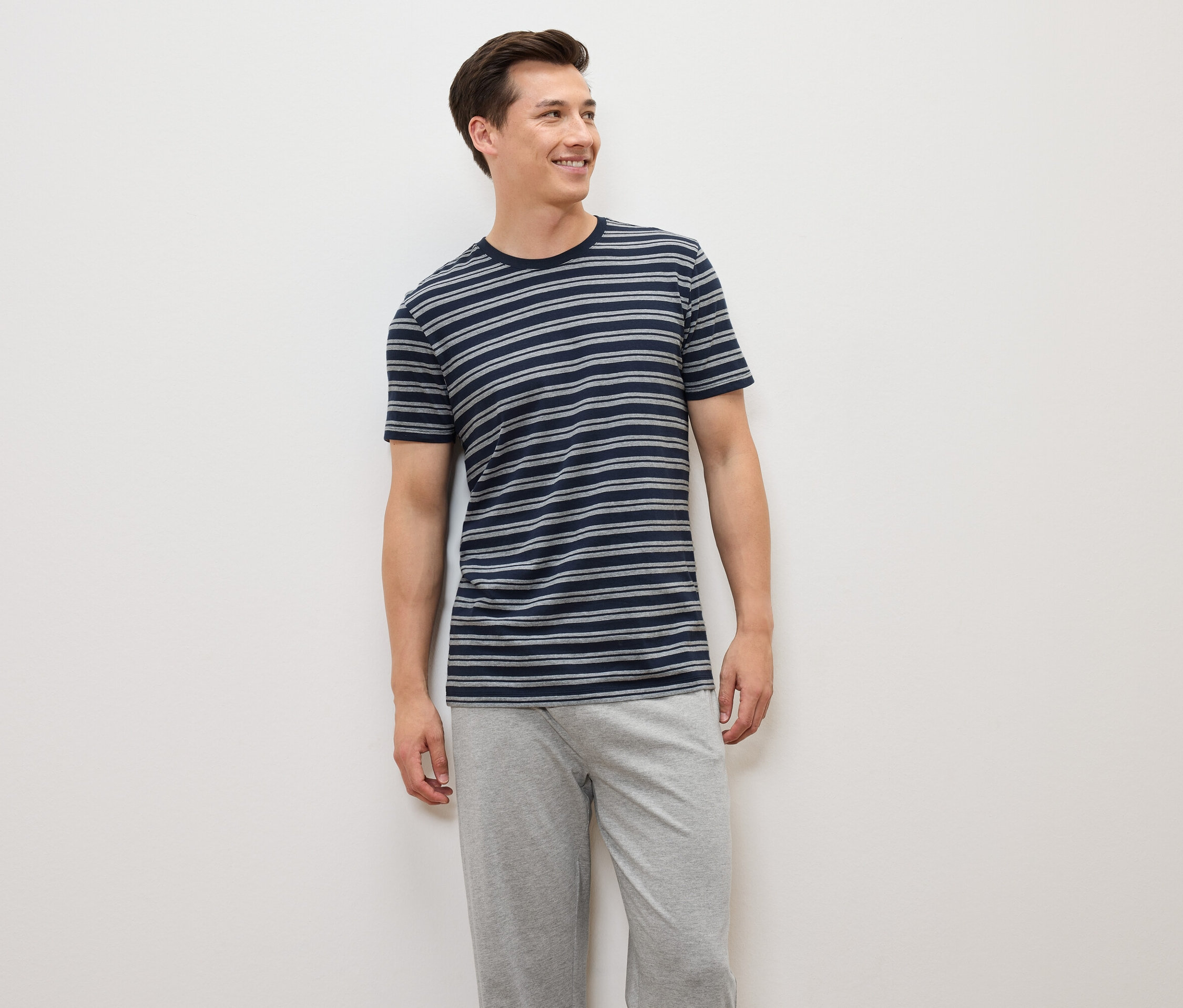 Un homme debout portant un t-shirt rayé bleu-gris et un pantalon gris.