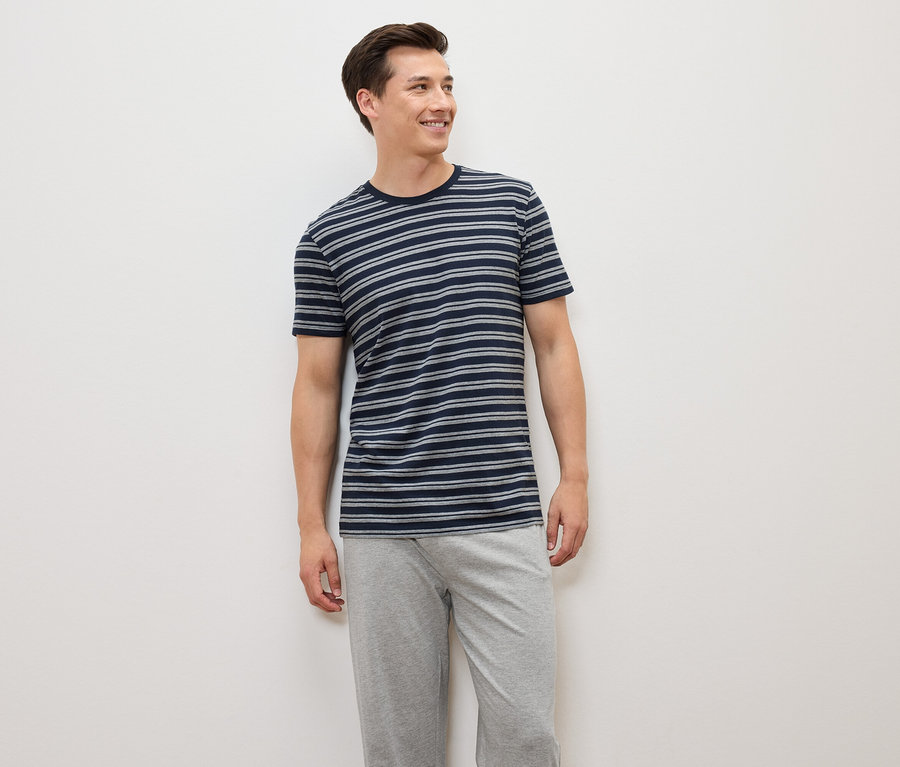 Un homme debout portant un t-shirt rayé bleu-gris et un pantalon gris.