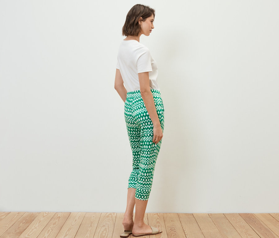 Une femme se tient de côté, portant un t-shirt blanc et un pantalon 3/4 en jersey imprimé.