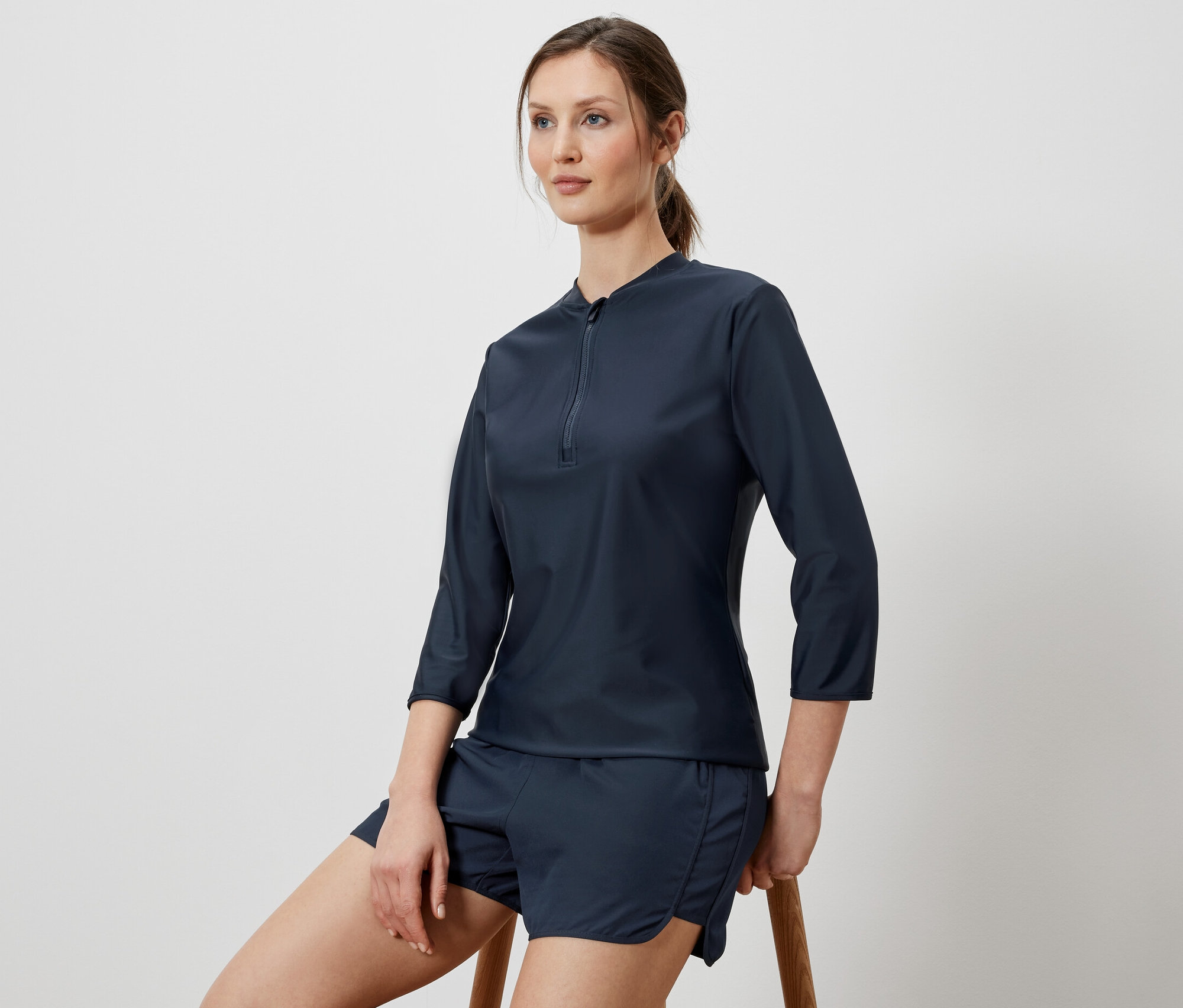 Une femme est assise sur un tabouret et porte un t-shirt de sport à protection UV et un short.