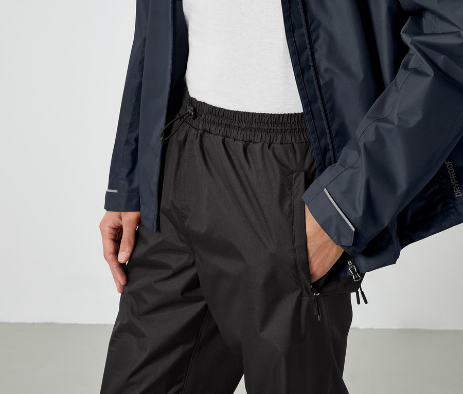 Un homme a une main dans la poche d'un pantalon noir et porte une veste bleue.