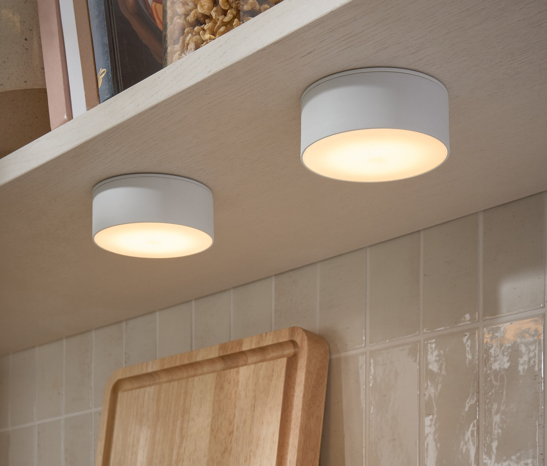 Deux lampes LED multifonctionnelles fixées sous une étagère. Sur l'étagère, il y a des bocaux de noix et des livres.