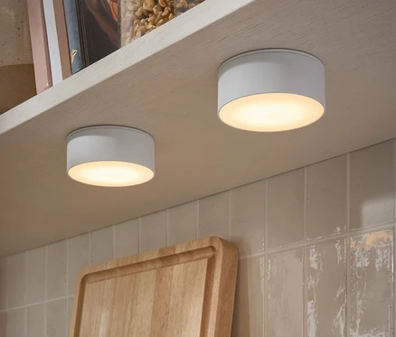 Deux lampes LED multifonctionnelles fixées sous une étagère. Sur l'étagère, il y a des bocaux de noix et des livres.
