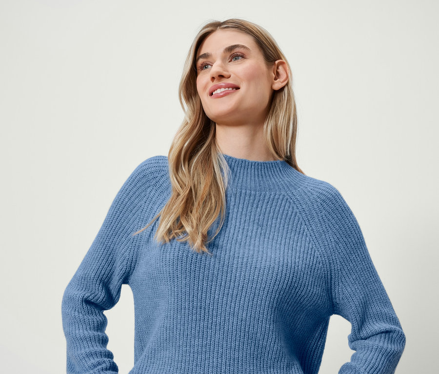 Une femme blonde souriante porte un pull bleu.