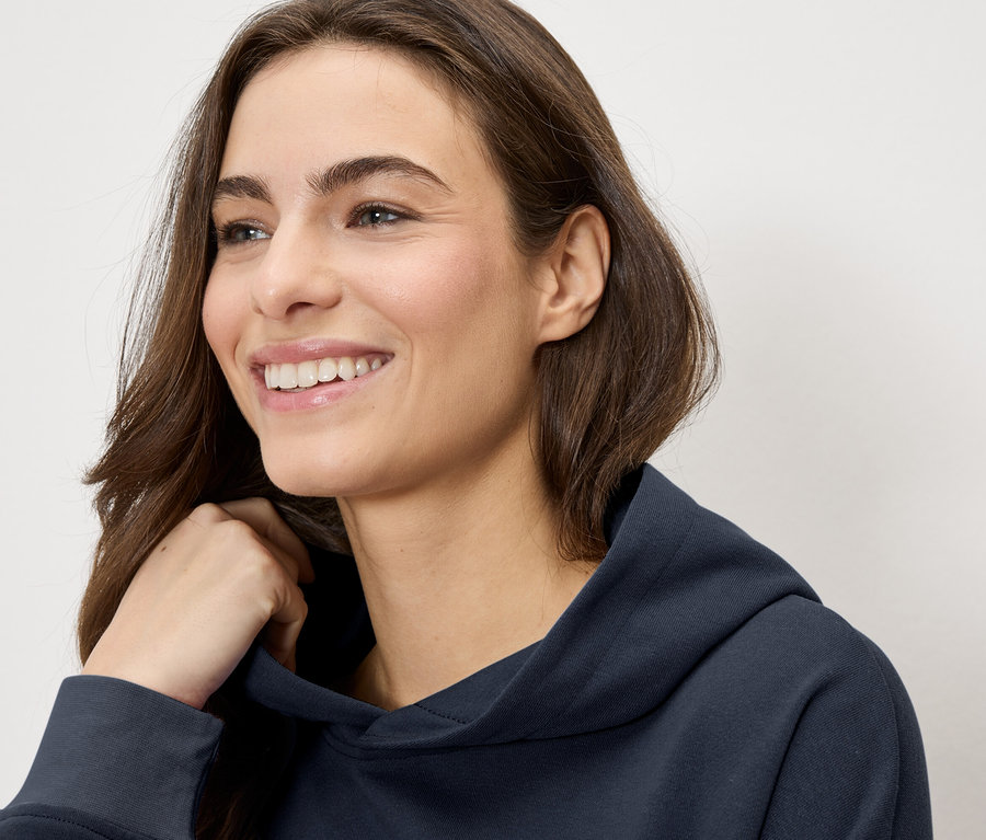 Femme souriante portant un sweat à capuche bleu marine.