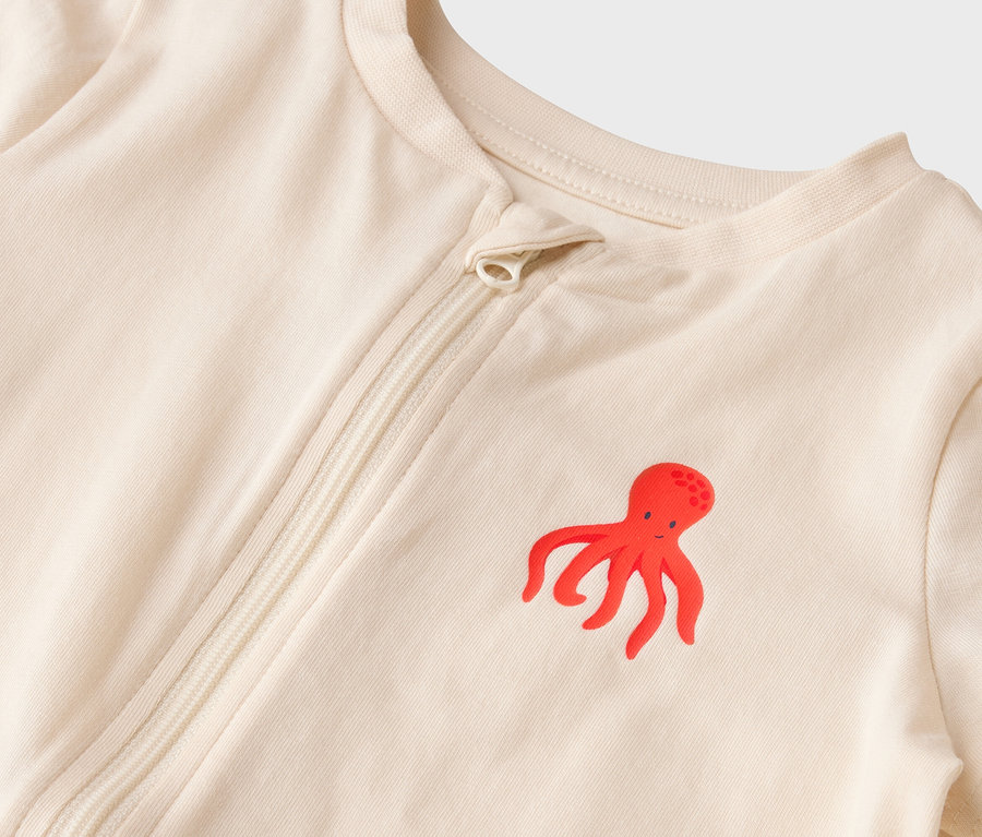Gros plan sur un pyjama de bébé beige clair avec un motif de poulpe rouge et une fermeture éclair.
