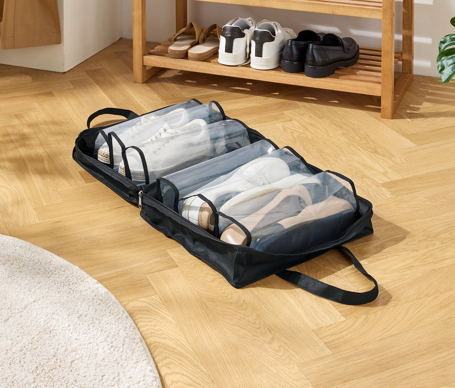 Un sac à chaussures noir avec plusieurs compartiments est posé sur un plancher en bois. Les compartiments sont remplis de différentes chaussures.