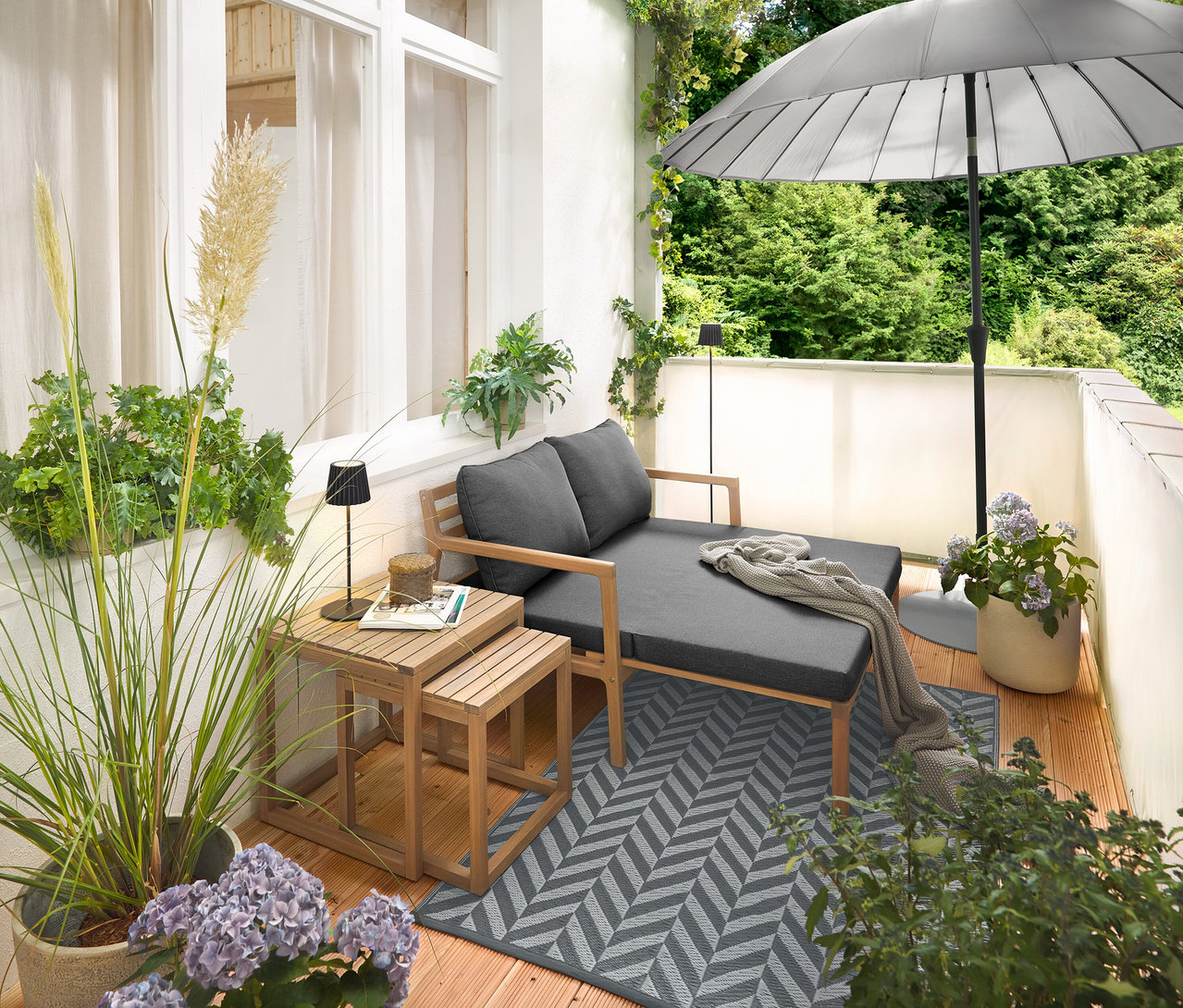 Aménagement sur un balcon avec un canapé de jardin extensible, un tapis d’extérieur (env. 165 x 115 cm), un brise-vue et brise-vent pour balcon de couleur crème, une lampe de table d’extérieur à LED rechargeable noire et un lampadaire d’extérieur à LED rechargeable noir.