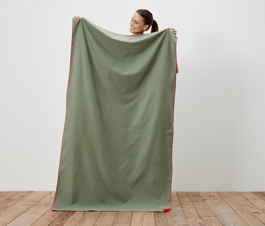Femme tenant une couverture vert olive avec une bordure rouge.