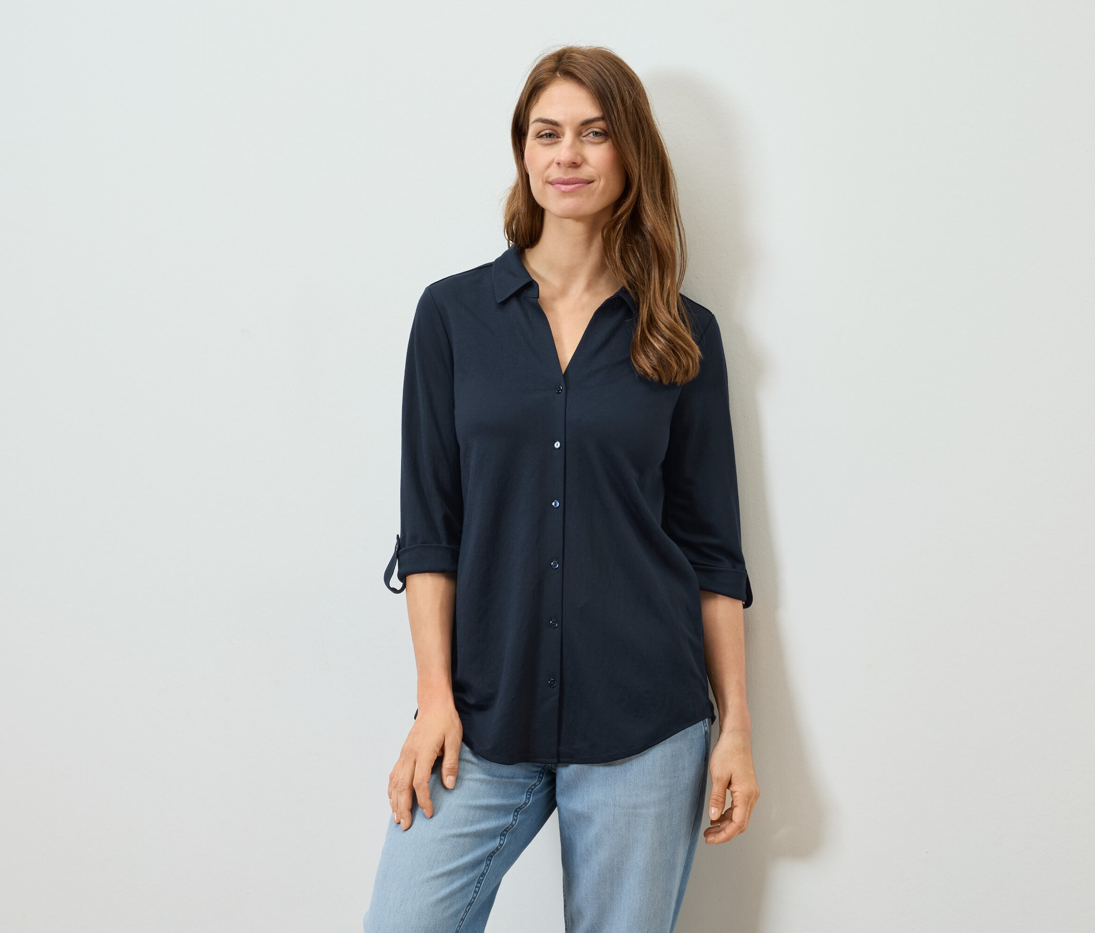 Une femme porte une chemise à manches longues bleu marine et un jean.