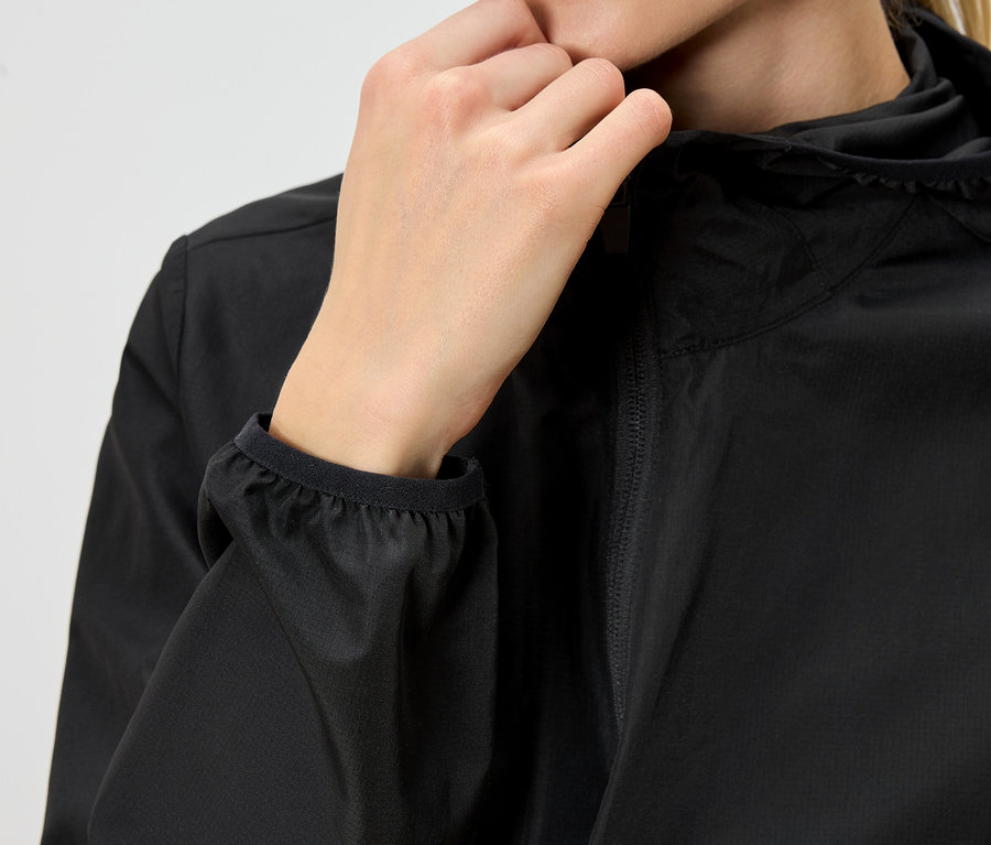 Gros plan d'une personne portant un imperméable noir à capuche et fermant la fermeture éclair avec sa main.