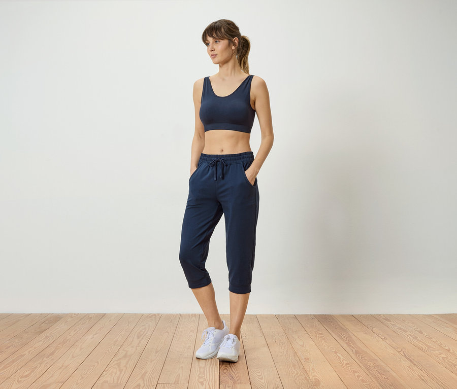 Femme portant un soutien-gorge de sport bleu marine et un pantalon bleu marine avec les mains dans les poches, portant des baskets blanches.