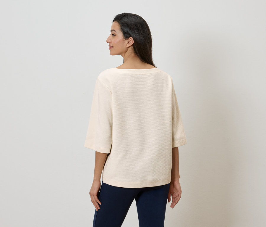 Vue de dos d'une femme aux cheveux foncés portant un haut ample crème et un pantalon bleu marine.