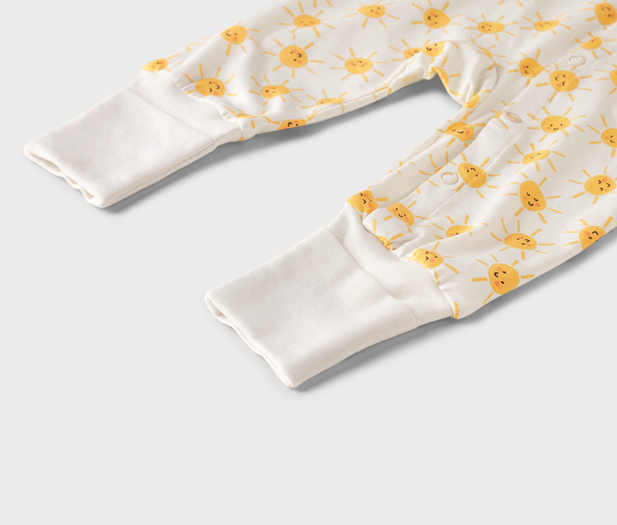 Gros plan sur une combinaison de bébé avec un motif de soleil jaune et des poignets blancs.