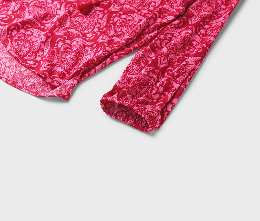 Gros plan sur un chemisier rouge à motif floral rose avec des manches longues.