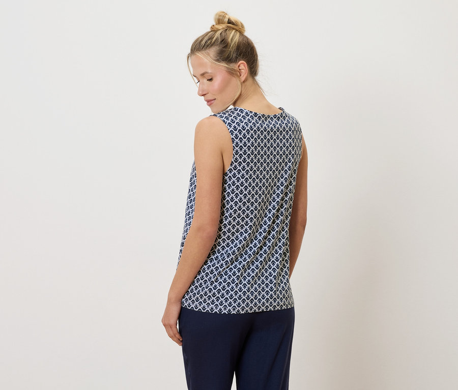 Vue de dos, une femme blonde portant un chignon porte un débardeur à motifs bleu et blanc et un pantalon bleu marine.