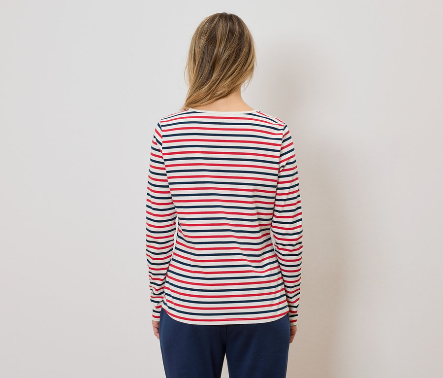 Vue de dos d'une femme aux cheveux blonds portant un t-shirt à manches longues rayé rouge, blanc et bleu et un pantalon bleu marine.