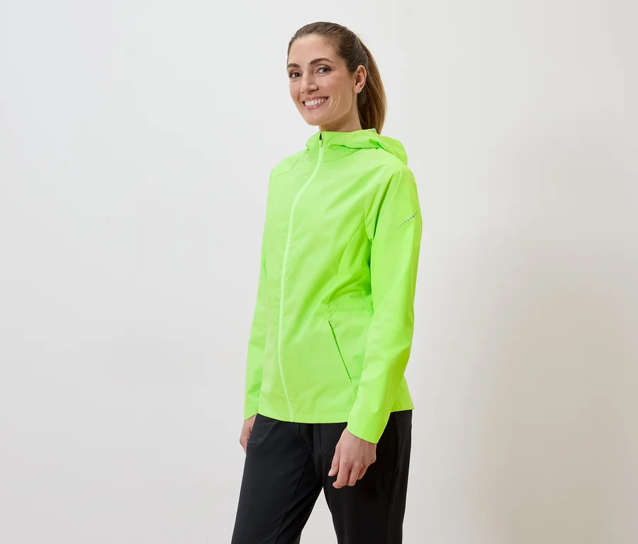 Une femme souriante portant une veste de pluie vert néon et un pantalon noir sur fond blanc.