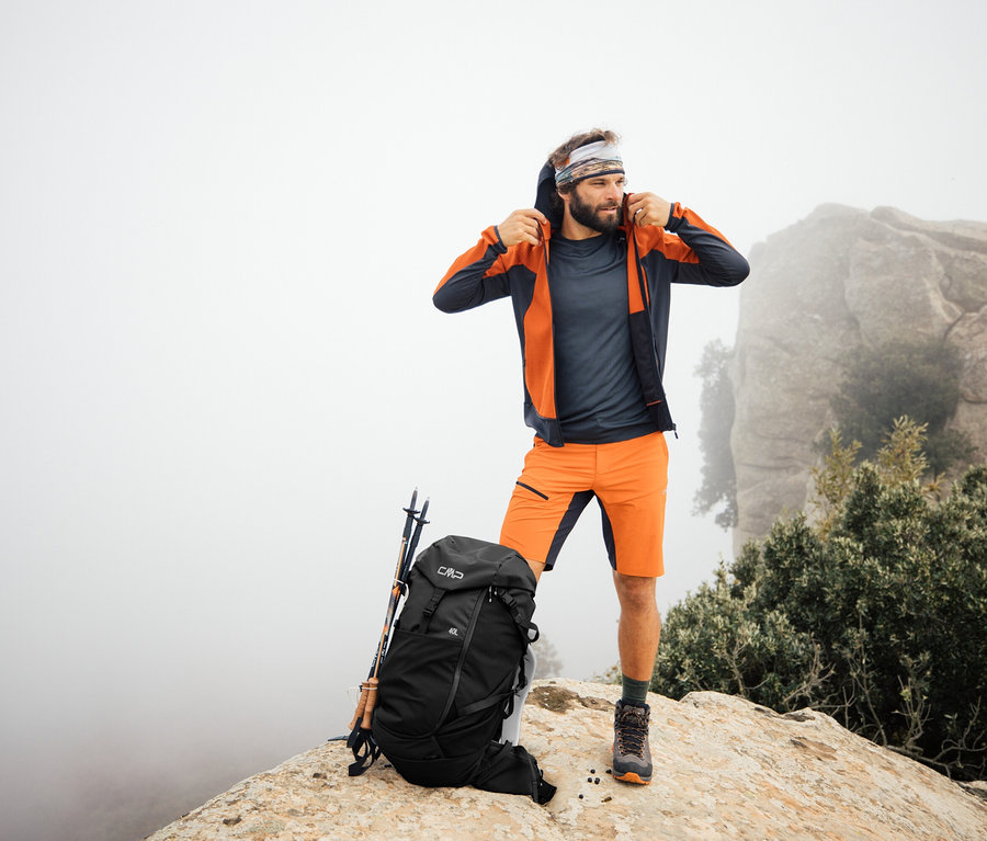 Un homme se tient debout sur un rocher avec un sac à dos de trekking CMP HAVRE de 40 litres. Des bâtons de randonnée sont appuyés contre le sac à dos.