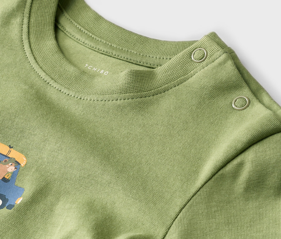 Gros plan sur un t-shirt vert clair avec un col rond, un imprimé et deux boutons sur l'épaule.