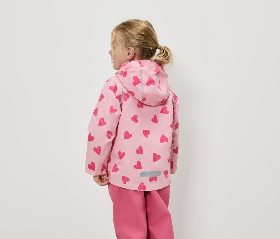 Vue arrière d'une petite fille blonde portant un imperméable rose à motifs de cœurs et un pantalon assorti.
