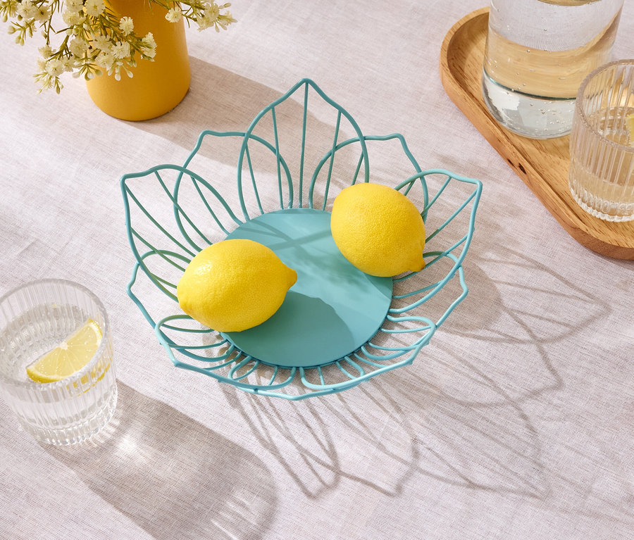Deux citrons reposent dans un panier en fil métallique bleu sur une table à côté d'un pot jaune avec des fleurs et des verres d'eau.