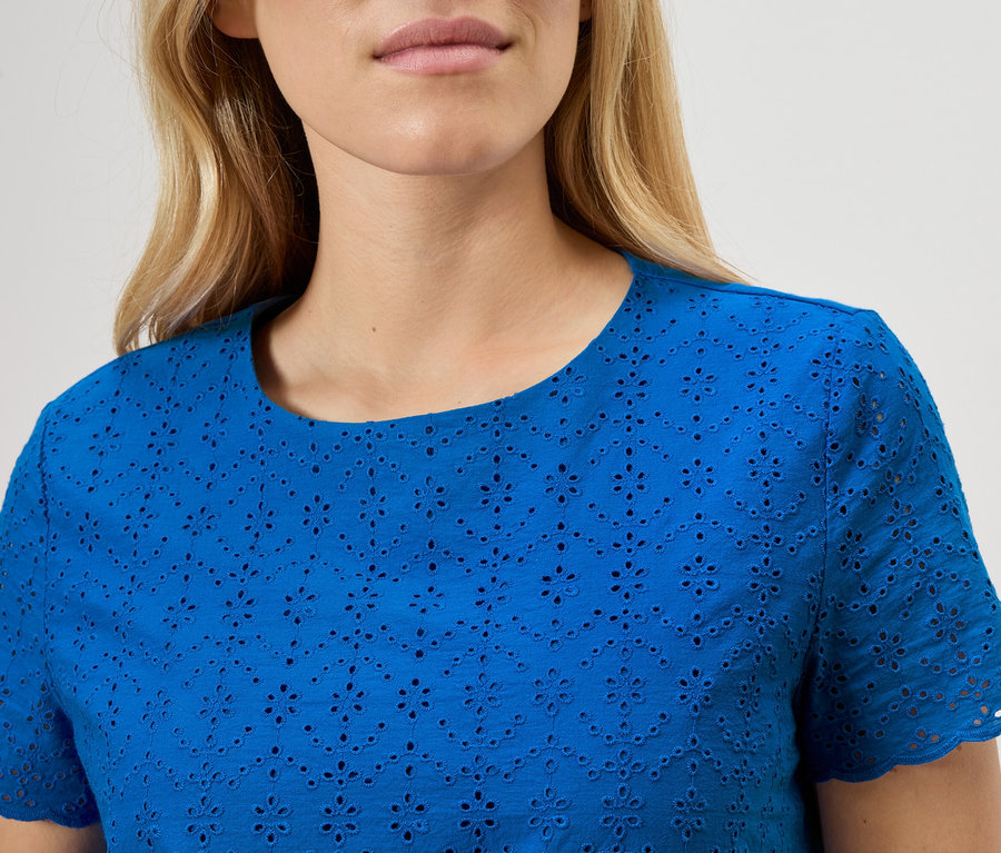 Gros plan d'une femme portant un haut bleu en broderie anglaise.