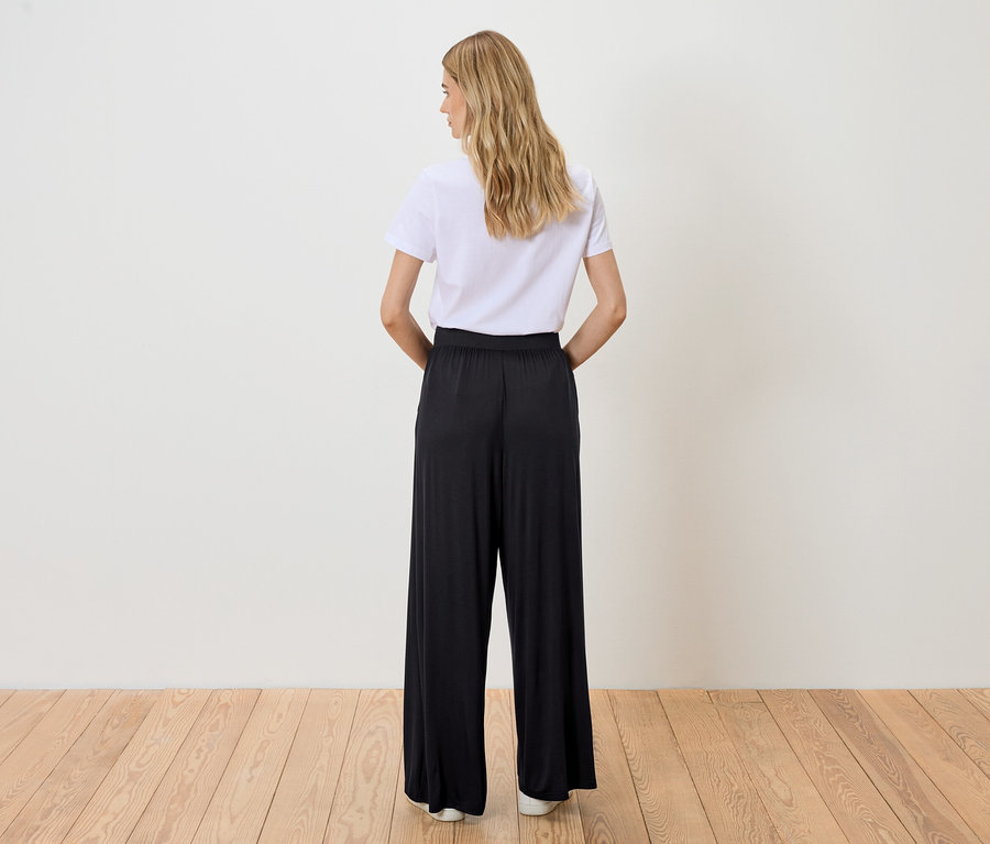 Femme vue de dos portant un t-shirt blanc et un pantalon noir.