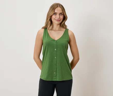 Une femme aux cheveux blonds porte un débardeur vert boutonné et un pantalon noir sur un fond blanc.