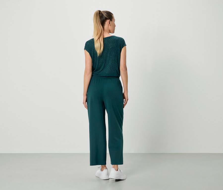 Femme vue de dos portant un haut et un pantalon vert foncé, avec des baskets blanches.